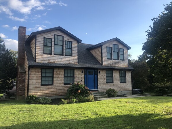 A two-story house with a blue front door, a brick chimney, and a well-maintained lawn. - Nonquit Cottage by Sakonnet Farm & Stays (Tiverton)