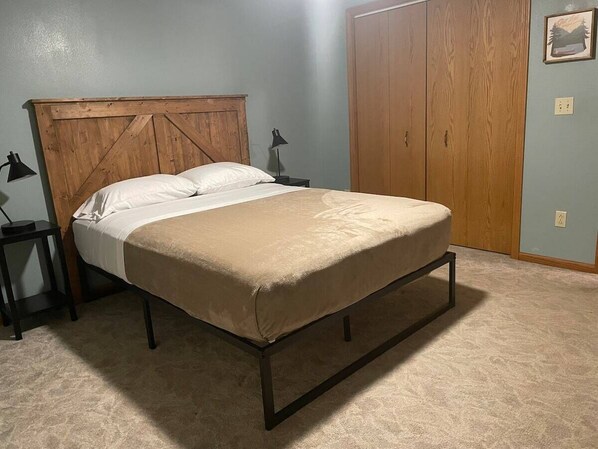 Una cama individual con cabecera de madera, una colcha color beige y dos mesitas de noche con lámparas.