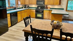 A modern kitchen with wooden cabinets, a black refrigerator, a microwave, and a stove. There is a dining table with chairs and a bowl of fruit. - Riverfront House near Cow Shoals - King bed & WiFi (Heber Springs)