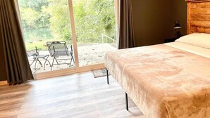 A bedroom with a large bed, a sliding glass door leading to an outdoor area with chairs and a table. - Riverfront House near Cow Shoals - King bed & WiFi (Heber Springs)