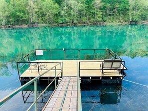 Un muelle flotante con dos plataformas, cada una con una mesa y sillas, rodeado de agua turquesa tranquila.