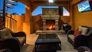 An outdoor patio with wicker furniture, a stone fireplace, and a television mounted on the wall. - Private Desert Oasis with Pool & Hot Tub, Game Room | Family & Pet Friendly (Scottsdale)