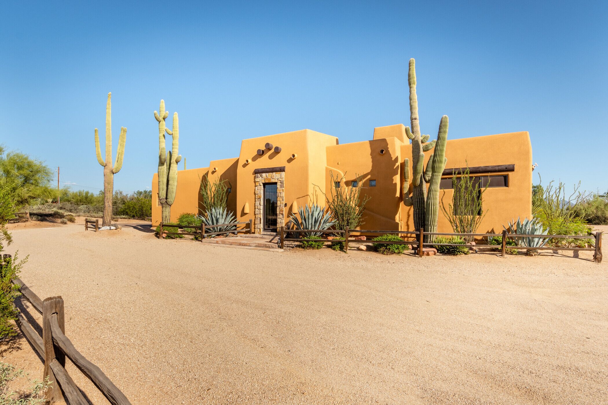 A desert-style building with a flat roof and stucco walls, surrounded by cacti and a gravel driveway.