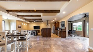 A spacious kitchen with a central island, a dining area with white chairs, and a large window providing natural light. - Private Desert Oasis with Pool & Hot Tub, Game Room | Family & Pet Friendly (Scottsdale)