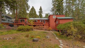 A cabin with a red exterior, a deck, and a stone pathway leading to the entrance.
