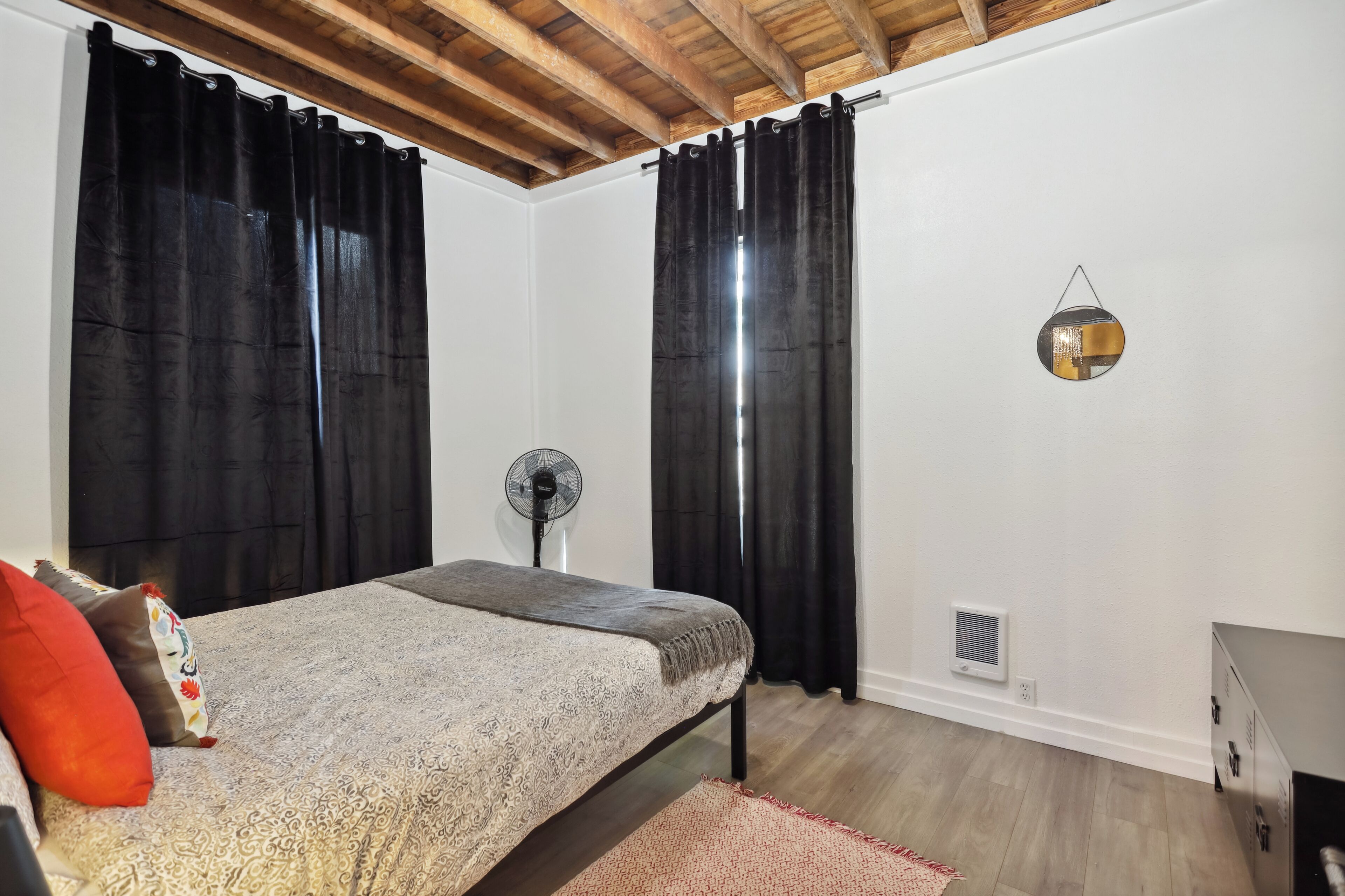 Un dormitorio con cama, cortinas negras, un ventilador y un pequeño calentador en la pared.