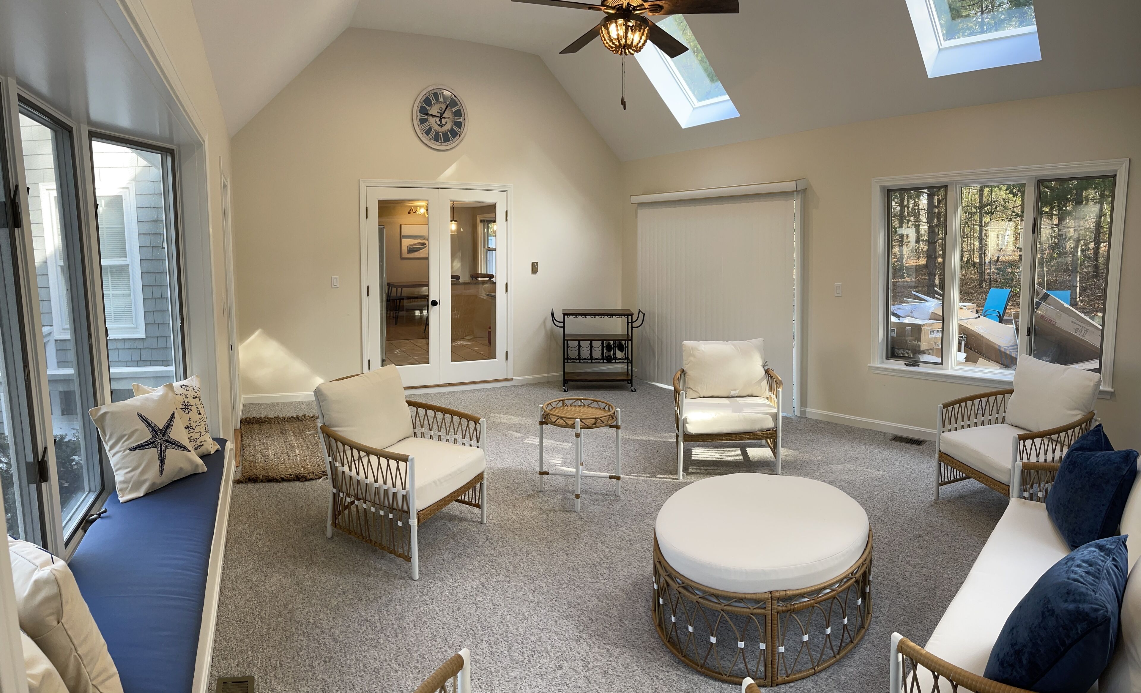 A spacious living room with a high ceiling, a ceiling fan, and large windows providing natural light.