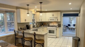 Una cocina moderna con armarios blancos, una isla central, taburetes de bar y una mesa de comedor.