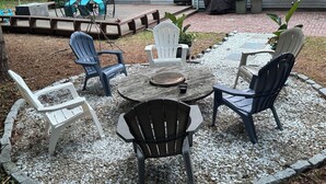 Un patio con sillas Adirondack, una mesa redonda y una zona de parrilla cubierta.