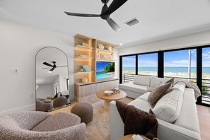 A modern living room with a large window, a ceiling fan, a built-in TV, and a cozy seating area.
