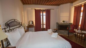 A hotel room with a large bed, a fireplace, a wooden ceiling, and a view of the outdoors. - Arkefthos Mountain Hotel (Zagori)