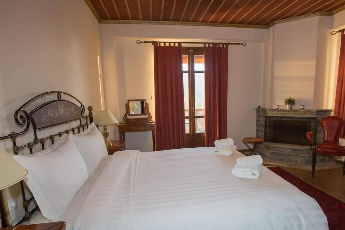 A hotel room with a large bed, a fireplace, a wooden ceiling, and a view of the outdoors.