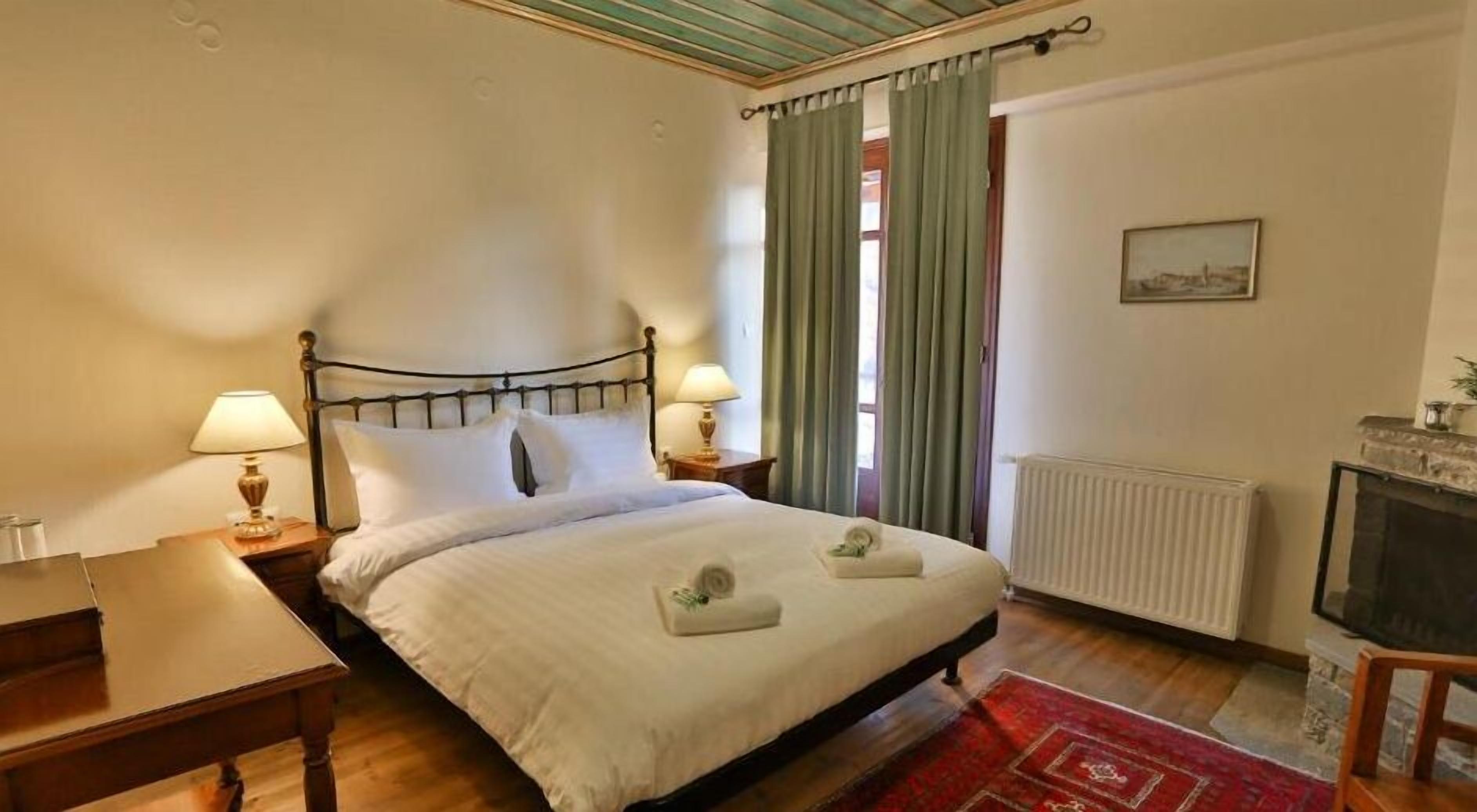 A neatly arranged hotel room with a bed, two bedside tables with lamps, a radiator, a fireplace, and a red rug.