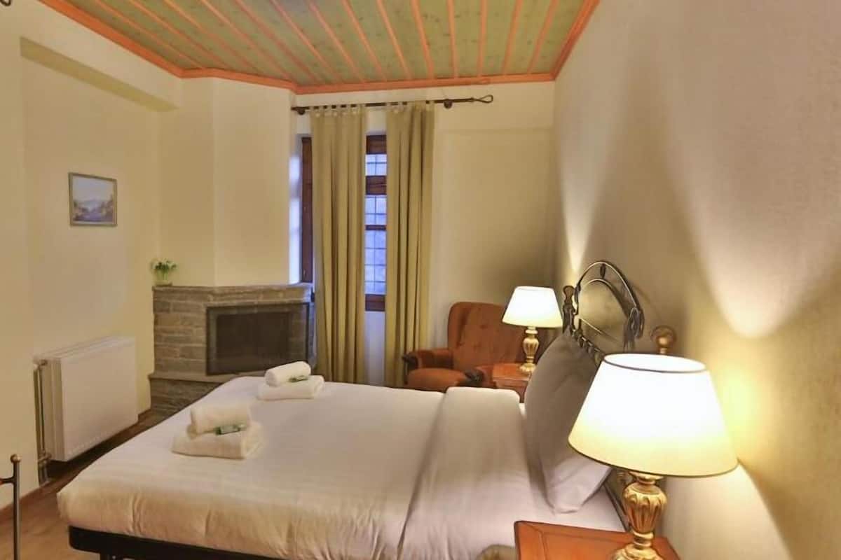 A hotel room with a bed, a chair, a lamp, a fireplace, and curtains.