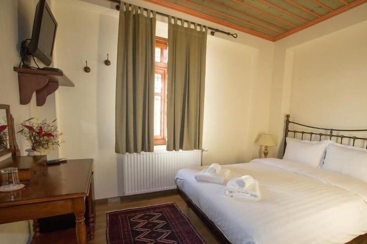 Een hotelkamer met een bed, nachtkastje, lamp en een raam met gordijnen.