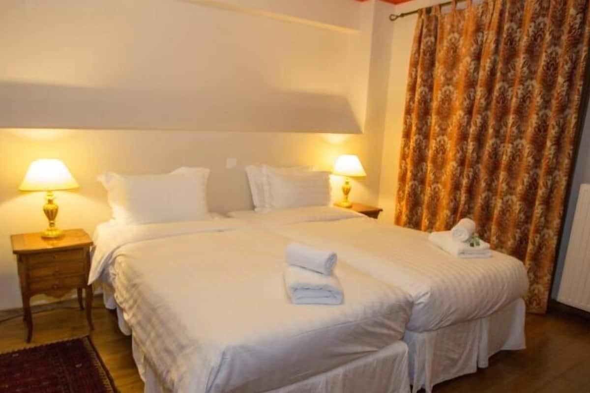 A hotel room with a double bed, two bedside tables with lamps, a patterned curtain, and a radiator.