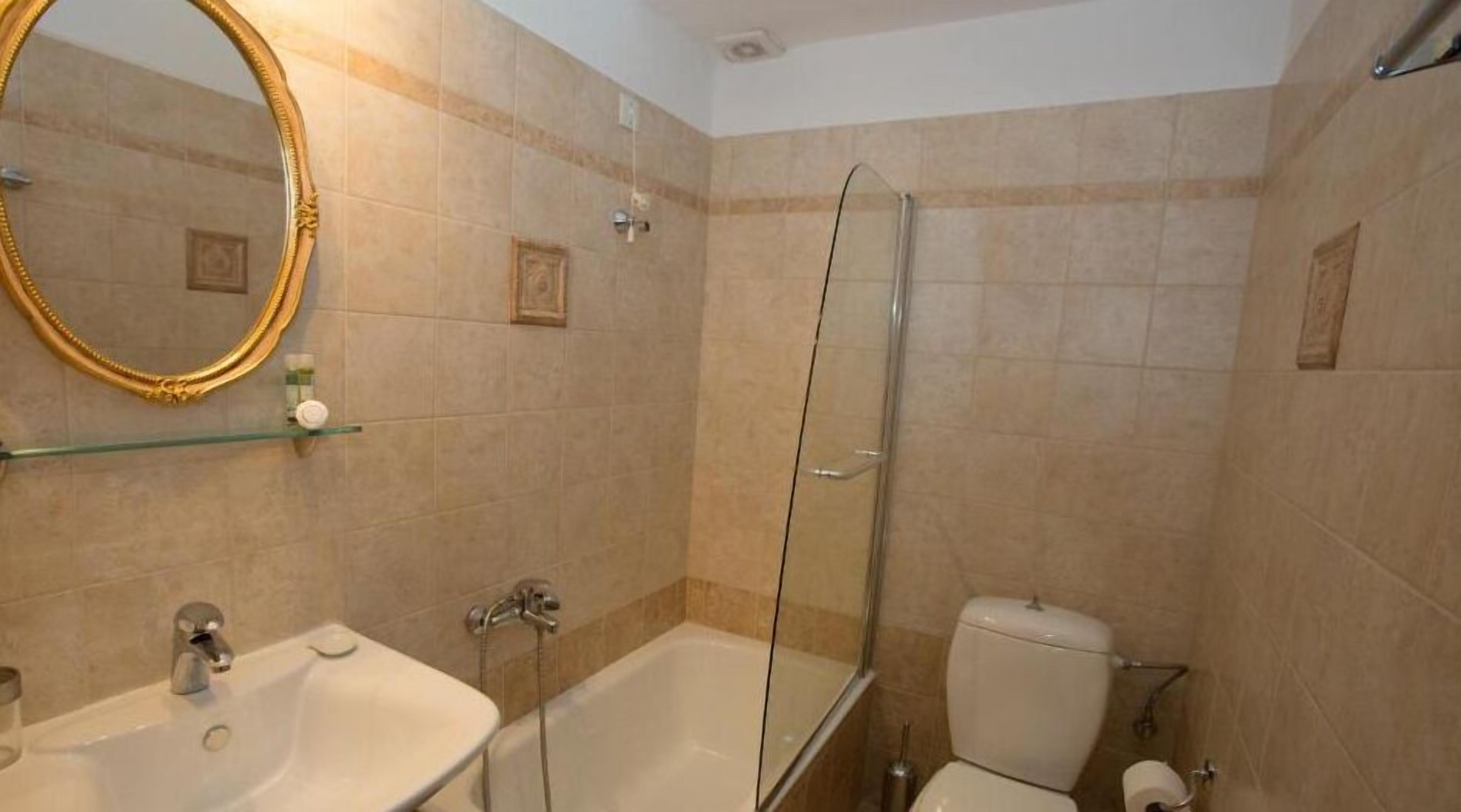 Un baño con bañera, inodoro, mampara de vidrio y lavamanos con espejo.