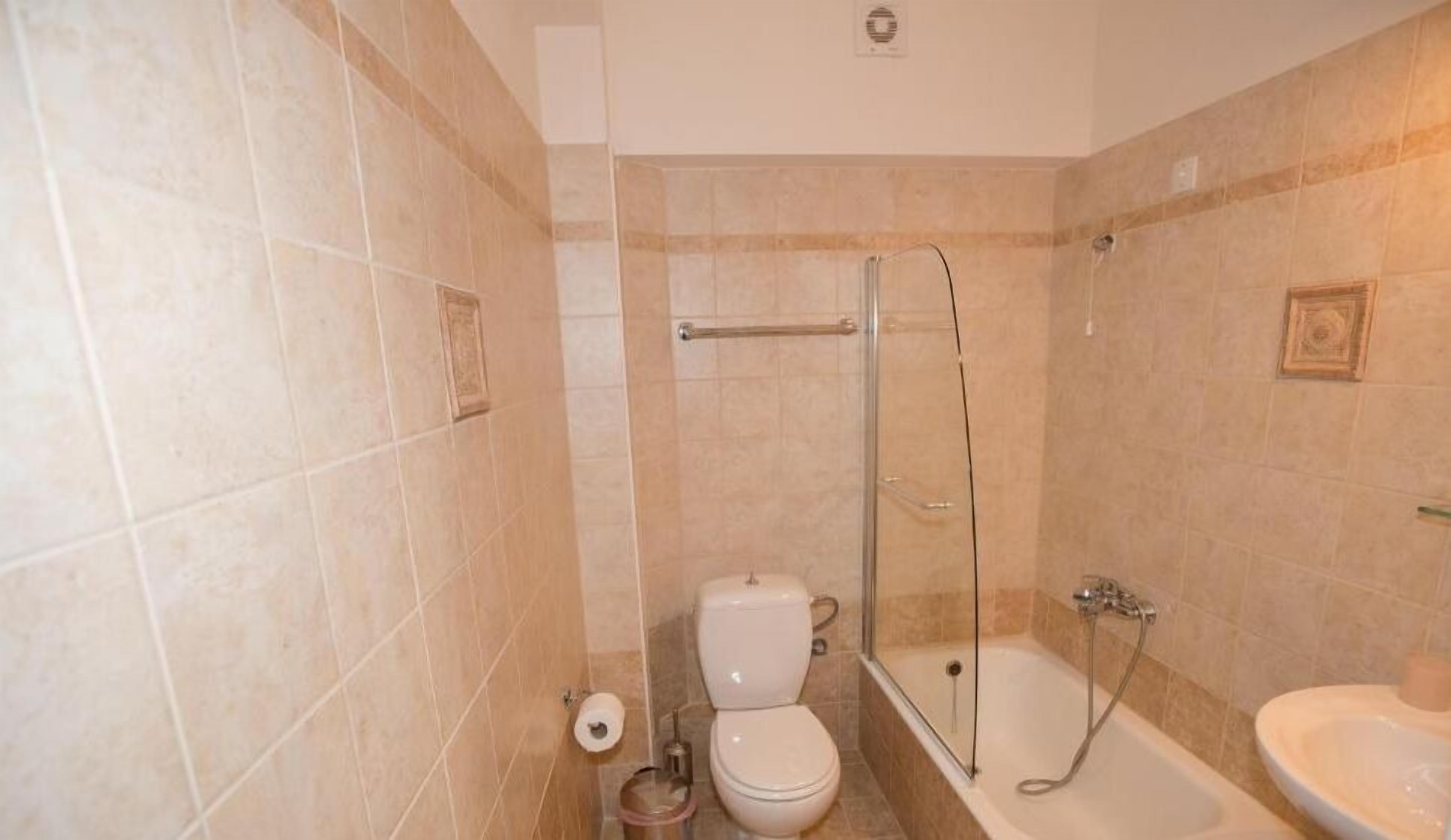 A bathroom with beige tiles, a toilet, a shower with a glass door, and a sink.
