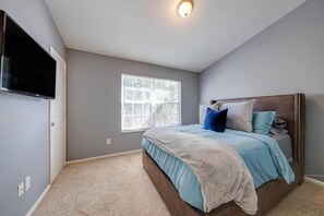 Un dormitorio con una cama grande, un televisor montado en la pared, una ventana y una lámpara en el techo.