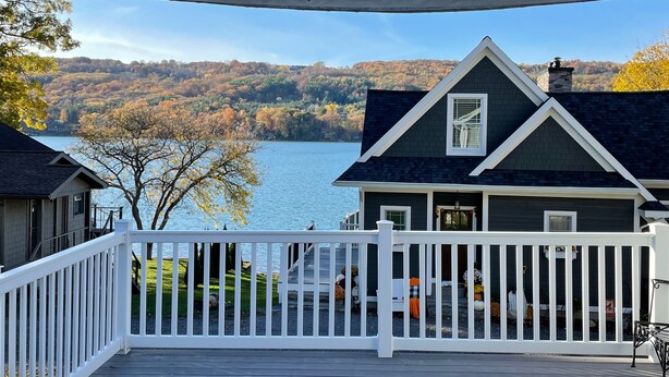 A house with a dark roof and white trim, overlooking a lake with autumn foliage. - Keuka East: Spacious & Comfy (Penn Yan)