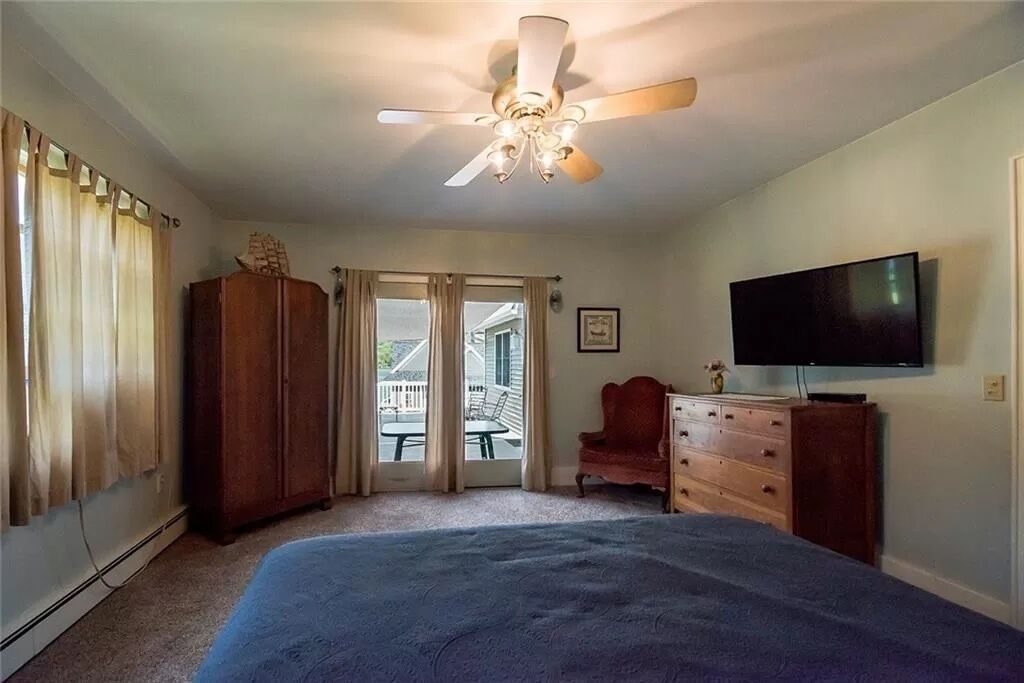 A bedroom with a bed, a ceiling fan, a TV, a dresser, and a window with curtains.