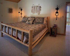 Un lit en bois avec une literie à motifs et une tête de lit, deux lanternes fixées au mur et une petite table de chevet en bois avec une pancarte.