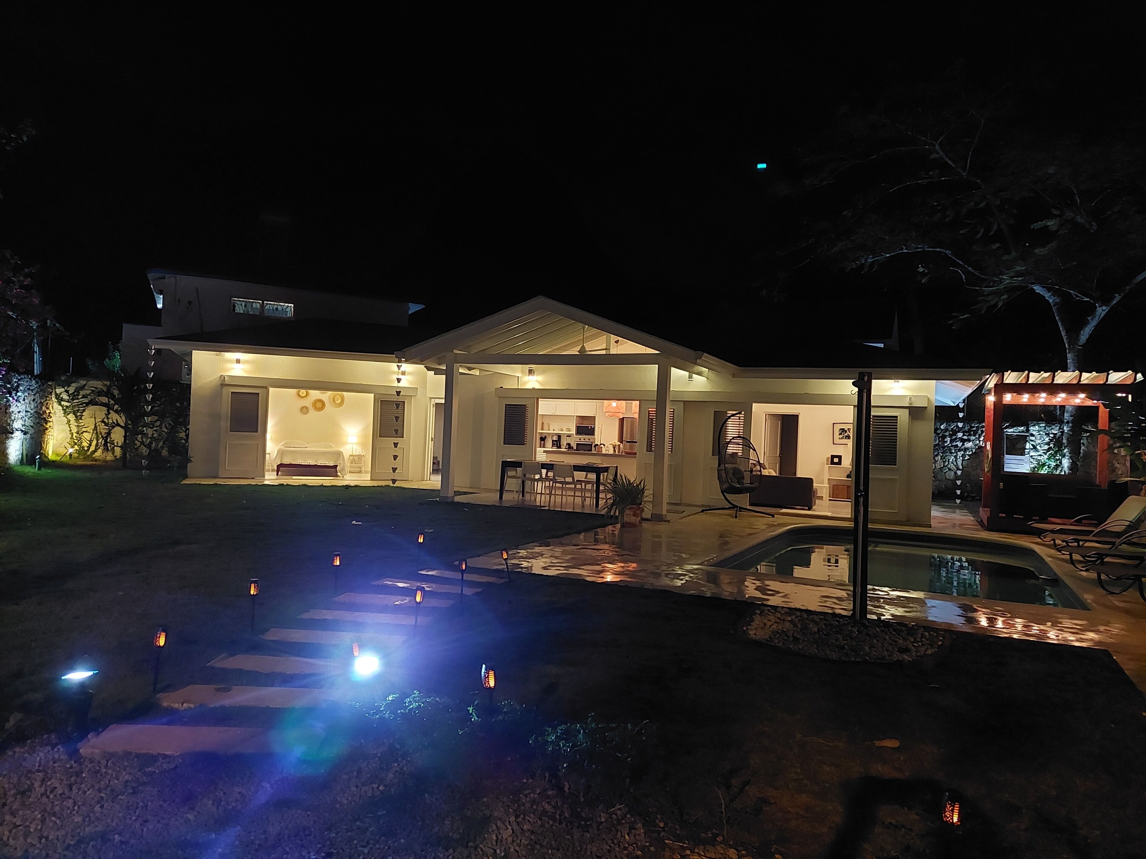 Una casa moderna con un patio cubierto, una piscina e iluminación exterior.