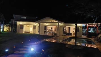 Una casa moderna con un patio cubierto, una piscina e iluminación exterior.
