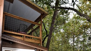 Un patio in legno con una griglia, un'area pranzo con sedie e una porta in vetro che dà su un ambiente interno.