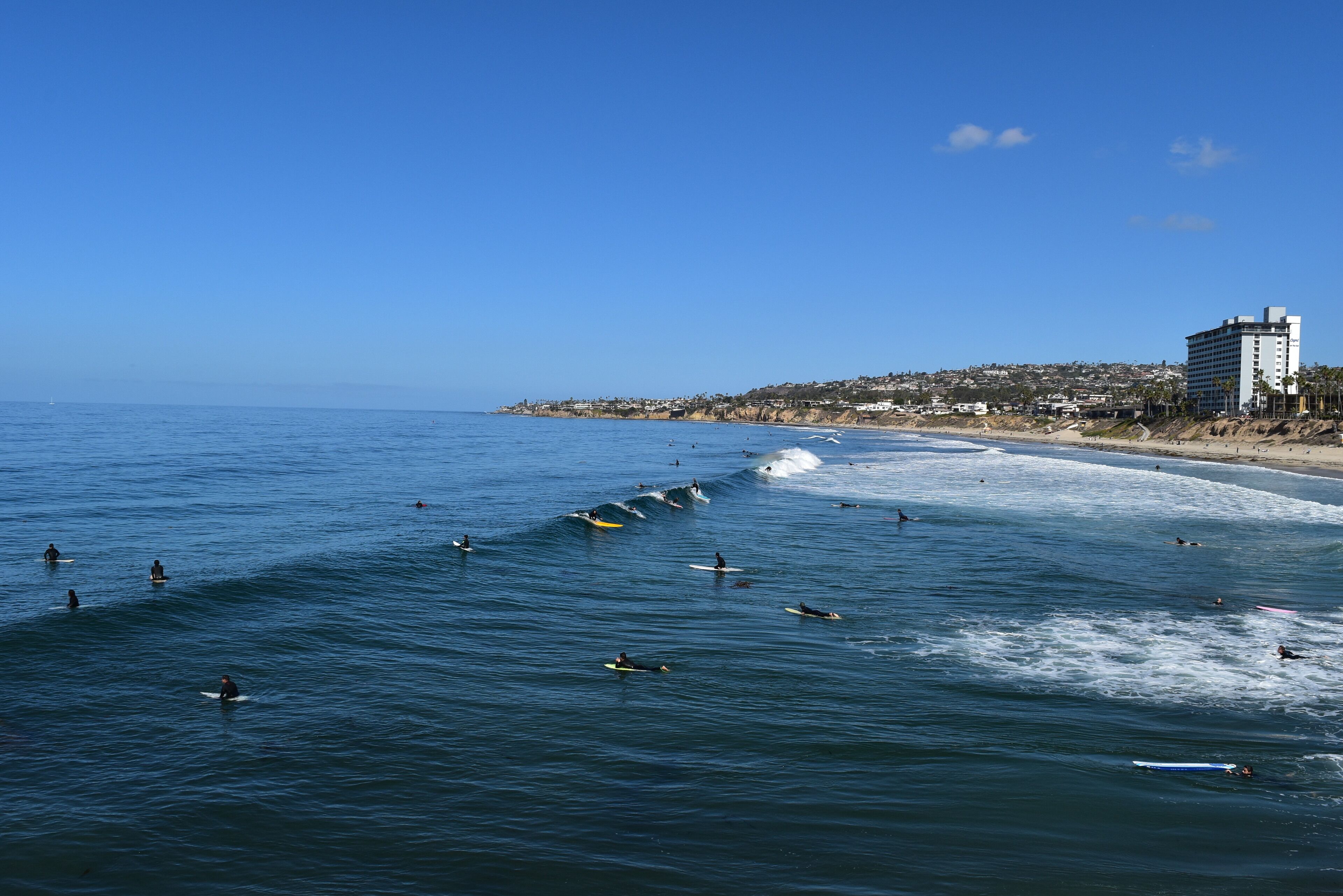 A coastal view with surfers on the water, a beach, and a building on the shore.