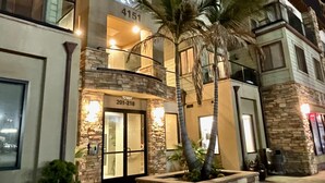Un hotel con fachada de piedra, un balcón con palmeras y una señalización con dirección visible.
