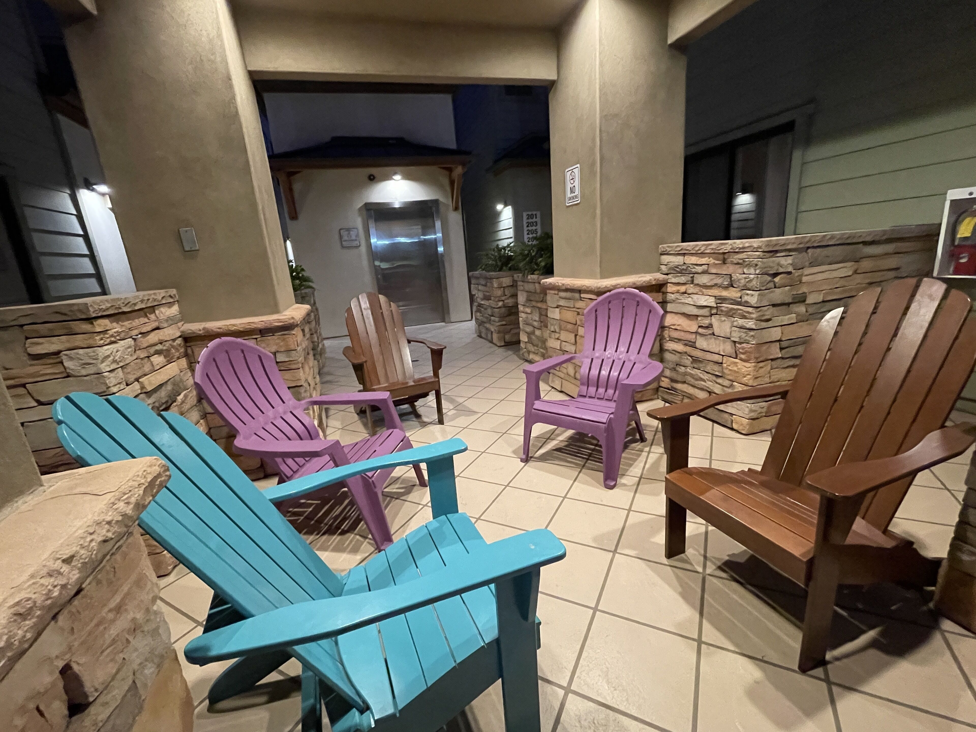 Uma área de pátio externa com várias cadeiras Adirondack em azul, roxo e marrom.