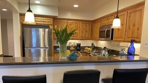 Una cocina moderna con armarios de madera, electrodomésticos de acero inoxidable y taburetes negros.