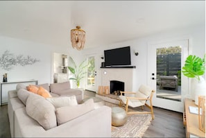 A modern living room with a sofa, armchair, fireplace, and a TV mounted on the wall. - Charming Spanish Bungalow, 2 blocks from the water! (Morro Bay)