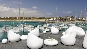 Un puerto deportivo con barcos, una playa de arena y zonas de estar blancas y modernas.