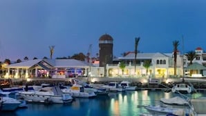 Un puerto deportivo con barcos amarrados, una torre destacada y edificios con letreros iluminados.