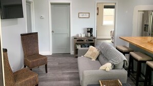 Een moderne woonkamer met een grijze bank, rieten stoelen, een koffiebar en een flatscreen televisie.