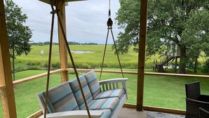 Een veranda met een schommelstoel met uitzicht op een grasveld en een boomhut.