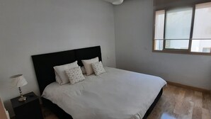 A bedroom with a bed, a nightstand, a lamp, and a window. - Large apartment Casablanca corniche (Casablanca)