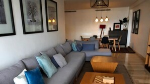 A modern living room with a grey sectional sofa, wooden coffee table, and a dining area with a table and chairs. - Large apartment Casablanca corniche (Casablanca)