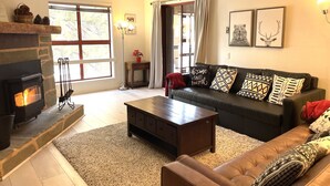 Uma sala de estar aconchegante com lareira, um sofá com almofadas estampadas, uma mesa de centro e um tapete.