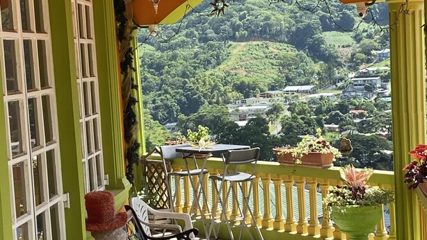 Un balcon donnant sur une colline verdoyante, avec une table et deux bancs.