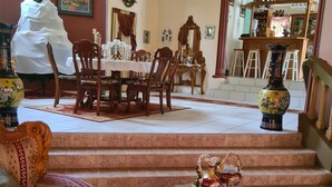 Un coin repas avec une table dressée pour quatre personnes, un escalier menant à un espace bar et un vase décoratif posé sur une table.