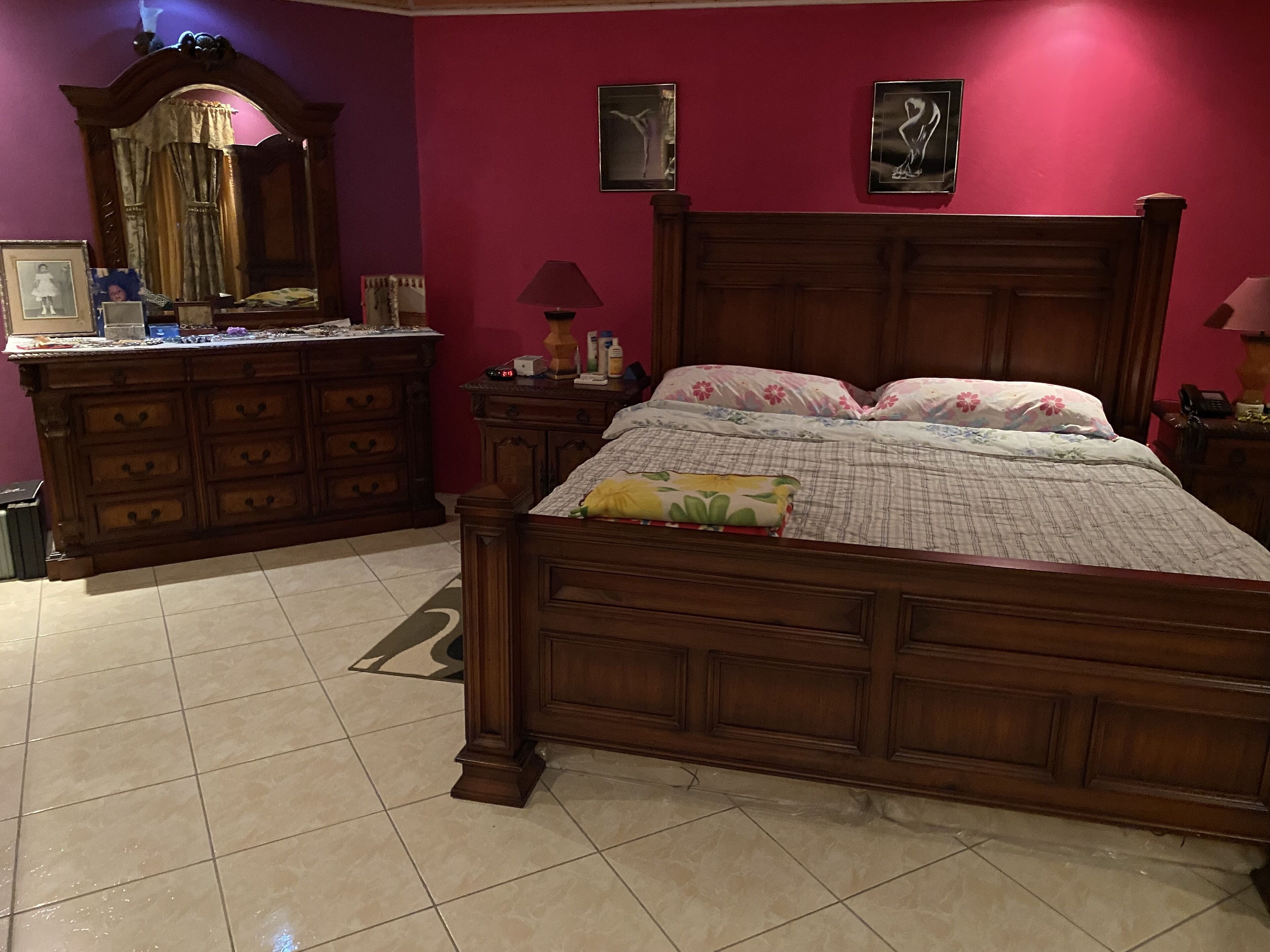 Un dormitorio con una cama de madera, un aparador, un espejo y dos cuadros en la pared.