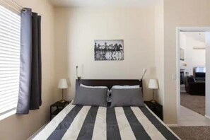 Un dormitorio con una cama, dos mesitas de noche, un tocador, una ventana con cortinas y un cuadro colgado en la pared.