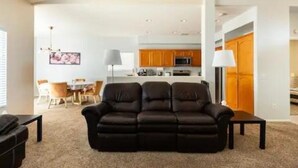 A modern living room with a black leather sofa, a dining area with a table and chairs, and a kitchen with wooden cabinets and a central island. - Family & Military-Friendly 4BR/2BA 
Near Camp Pendleton, Legoland & Coastal Fun (Oceanside)