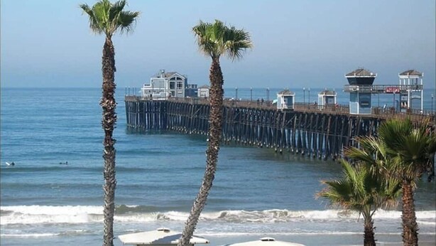 A pier extending into the ocean with a building at the end. Palm trees are visible in the foreground. - Family & Military-Friendly 4BR/2BA 
Near Camp Pendleton, Legoland & Coastal Fun (Oceanside)