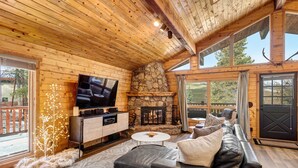 L’intérieur d’un chalet confortable, avec une cheminée en pierre, un téléviseur, un canapé en cuir et de grandes fenêtres.
