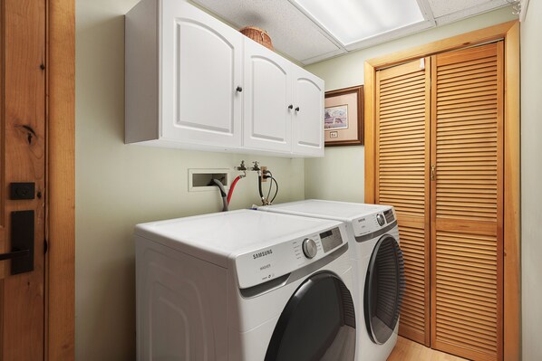 Un cuarto de lavandería con lavadora y secadora Samsung, armarios de madera y una puerta de madera.