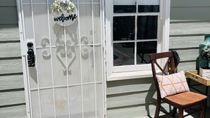 Una puerta blanca con un letrero que dice 'welcome', una silla de madera con cojín y un felpudo con la frase 'Come in and say hi up'.